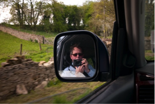 Phot of a man taking a photo of himself in a car mirror