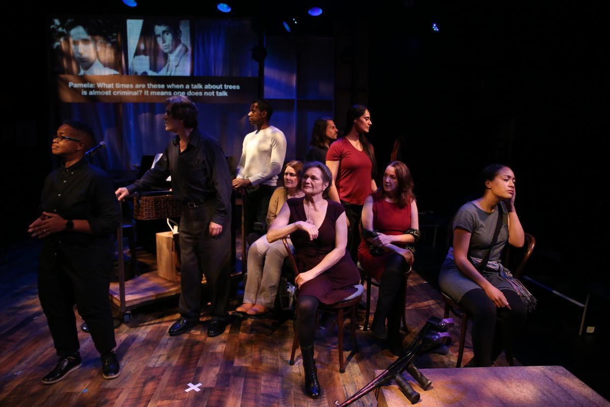A picture of the cast of Brecht on Brecht. Everyone is sitting and standing and looking in different directions. Behind them, we see a screen with texts and pictures on it.