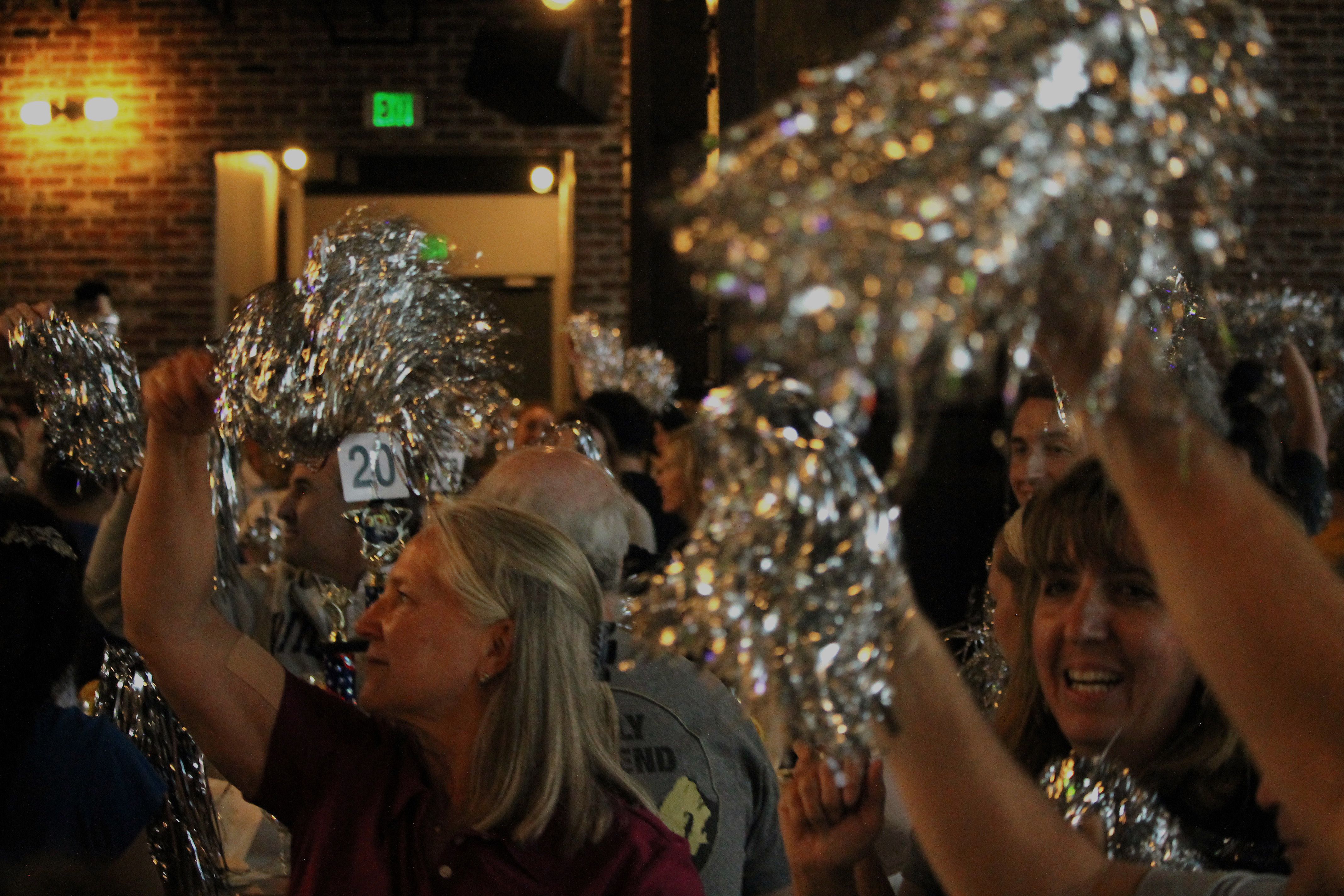 Crowd of people in banquet hall waving silver pom poms