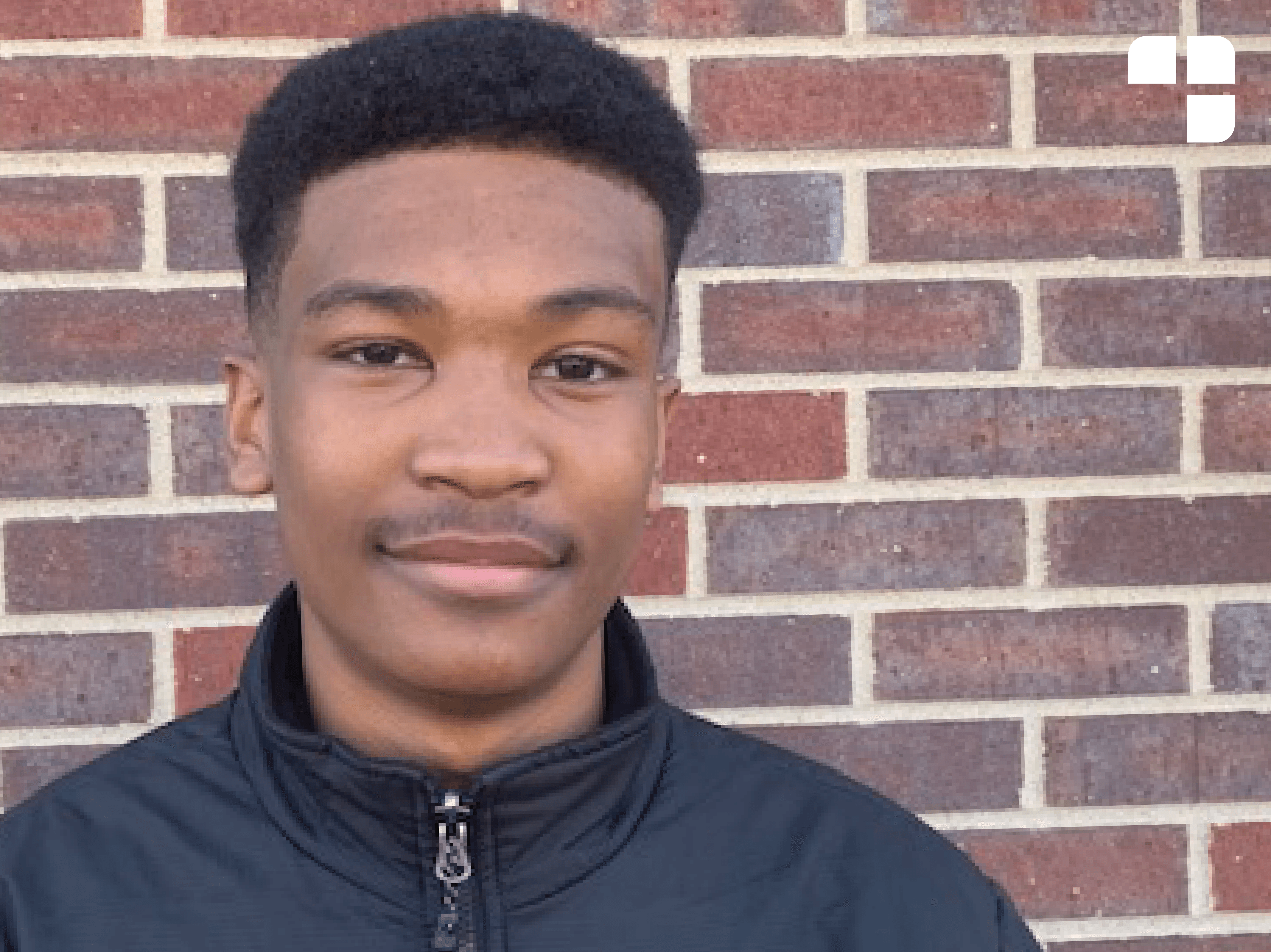 Hasani stands in front of the brick wall.