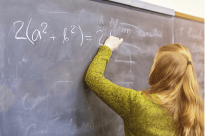 Female high school student wearing a sweater working out a math equation on a blackboard