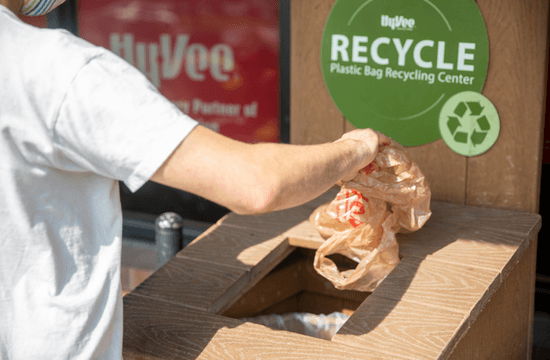 a person puts a plastic grocery bag into a container for bag recycling in front of the store