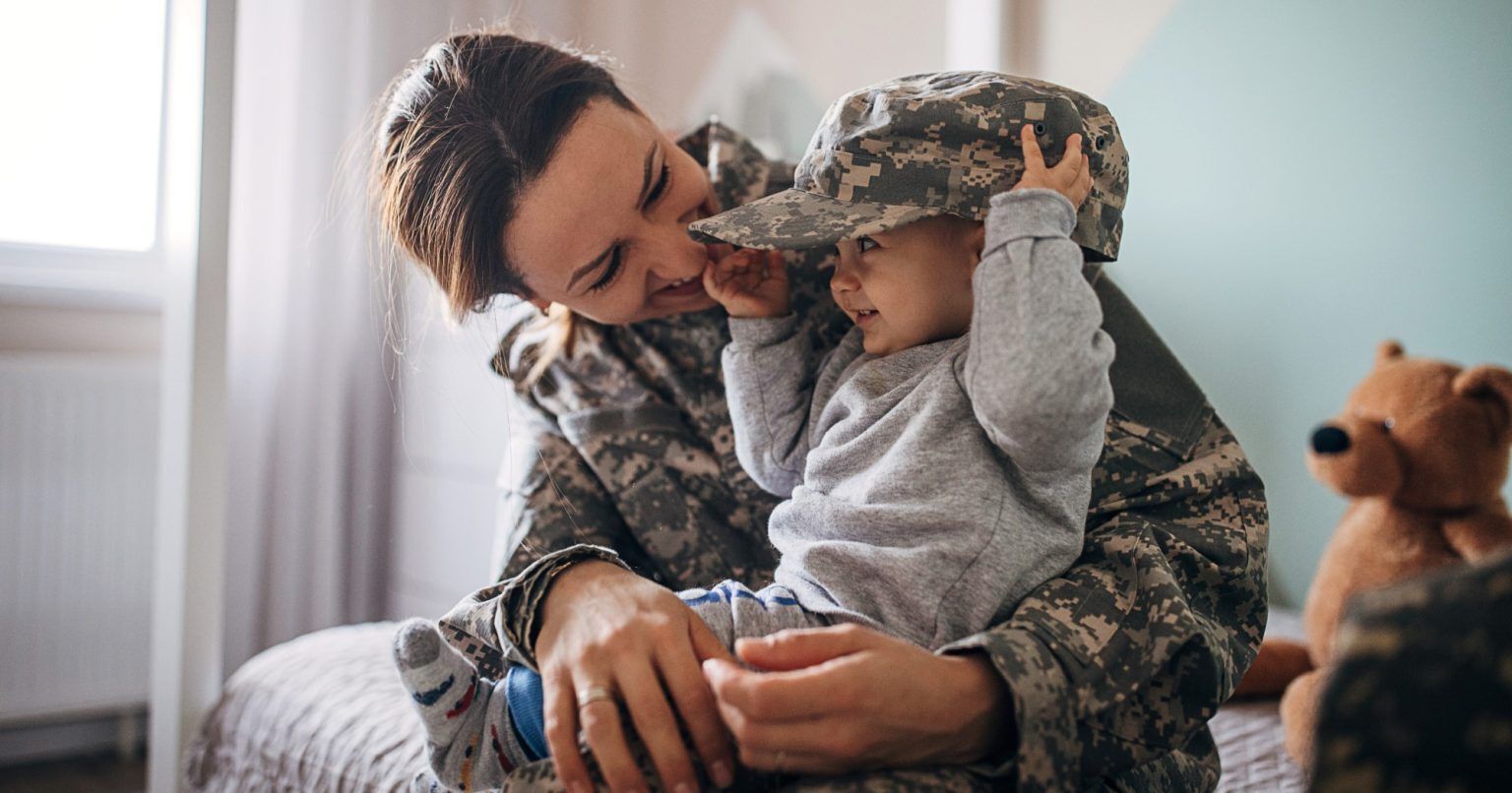 Mom in military uniform holding her infant child who is wearing her camouflage hat