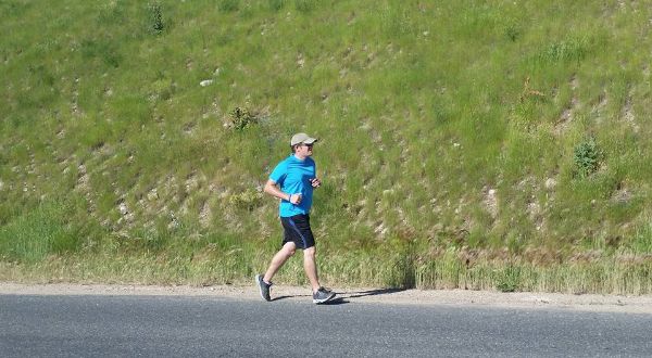 Photo of Ryan running on the road in front of a grassy hill