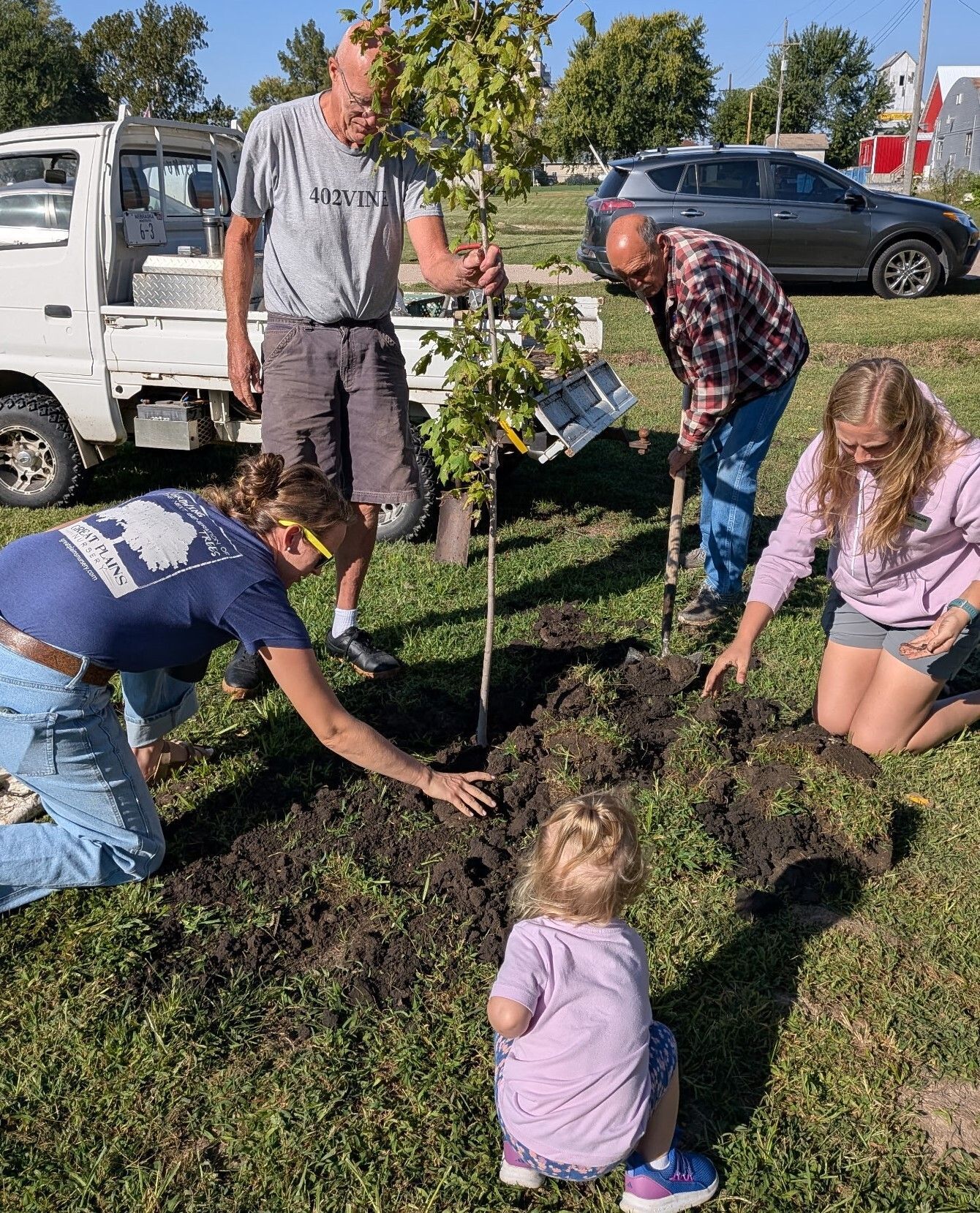 A group of men and children volunteers plant an oak tree.