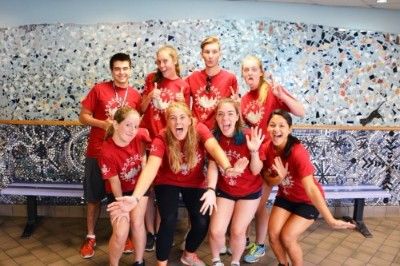 Image of 8 students wearing red shirts posing in SpArc's lobby in front of a blue mosaic wall., 