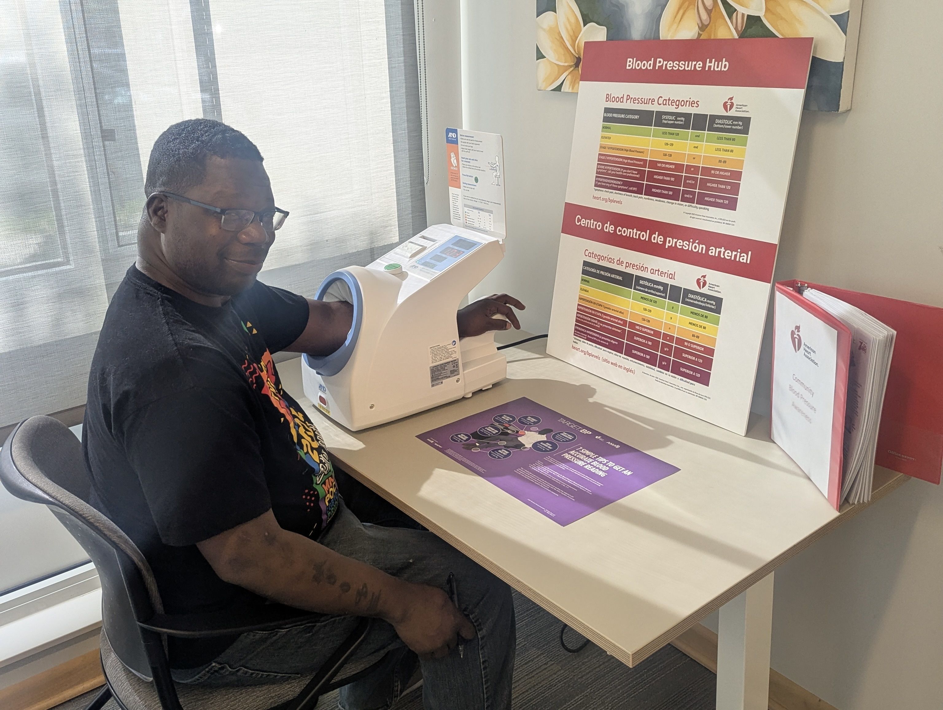 A man sitting at a table with his arm in a blood pressure cuff in front of educational materials