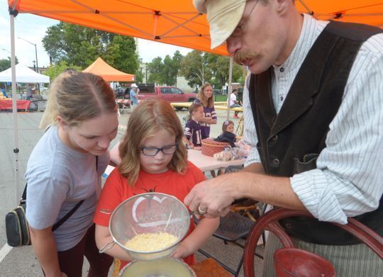 Male historic reenactor showing two children how to sift ground corn at the Smoky Hill Museum Street Fair.