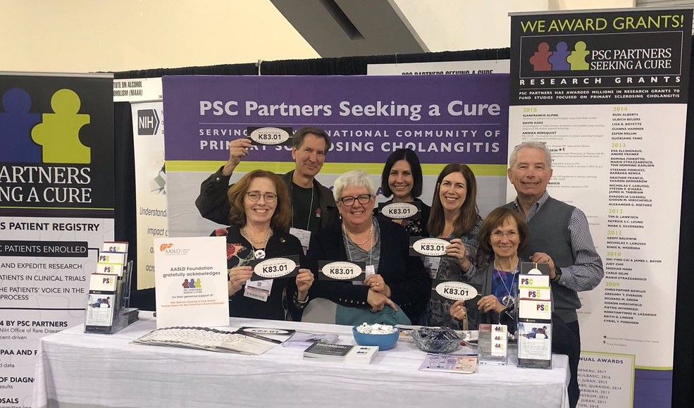 A group of seven people stand at a PSC Partners booth. All of them are smiling and holding up PSC ICD-10 postcards.