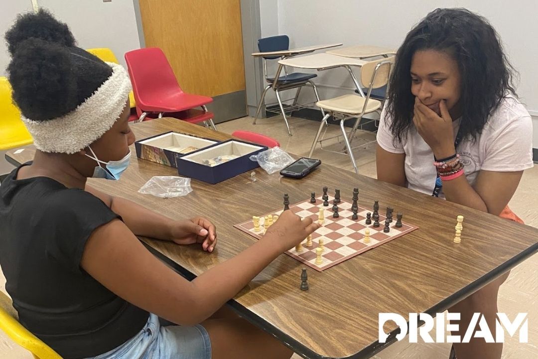 A girl and her mentor, also a woman, playing chess, expressing happy looks on their faces