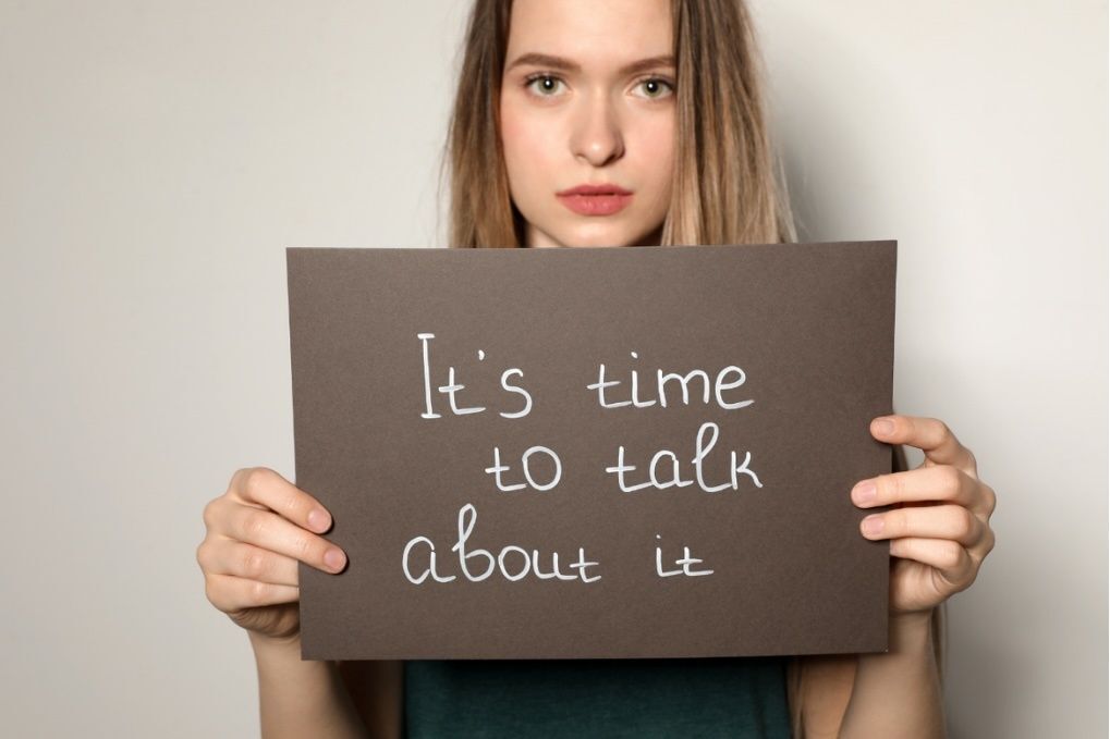 A girl holding up a sign that says " We need to talk about it"