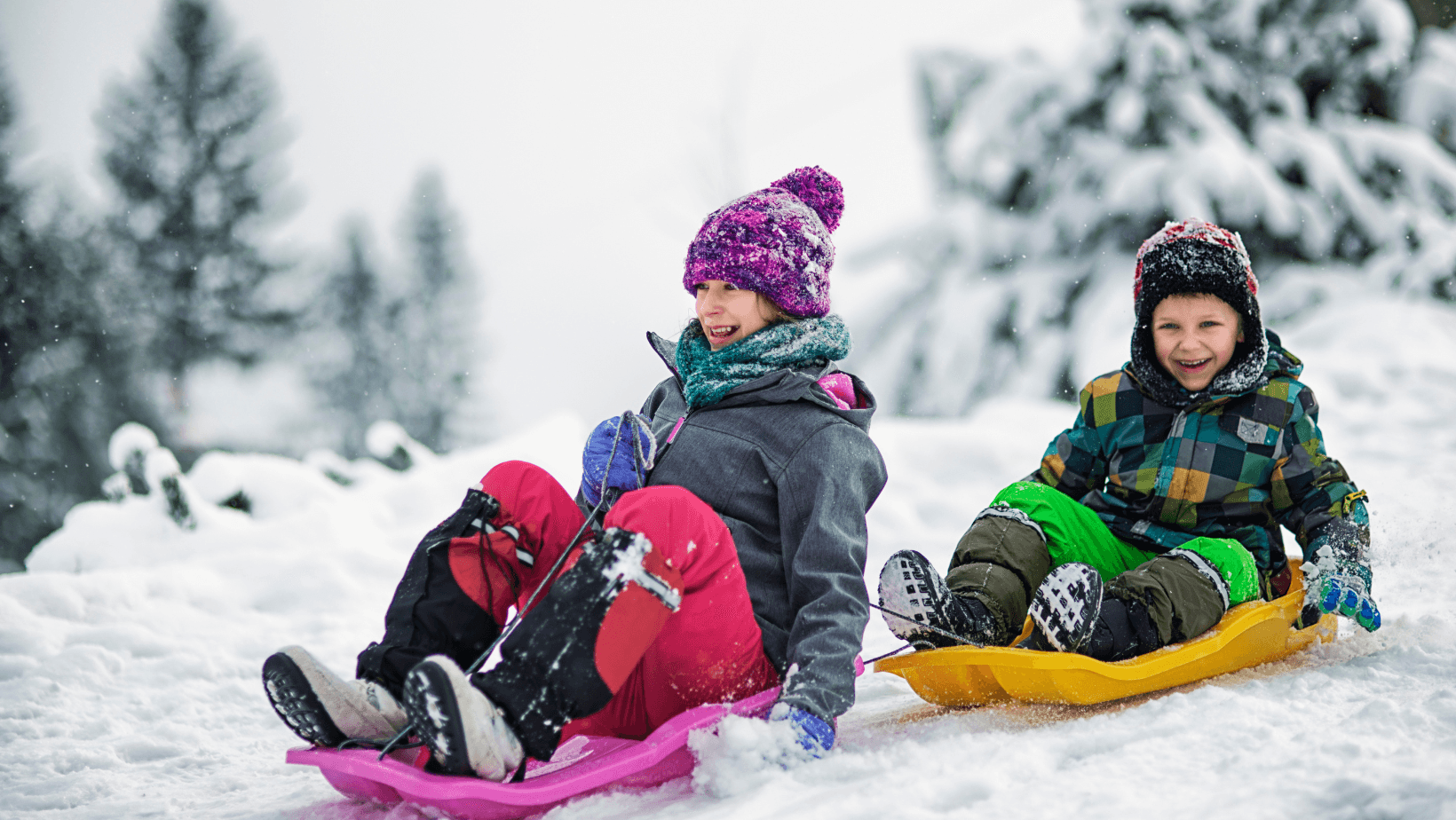 Two children sledding with winter clothing on