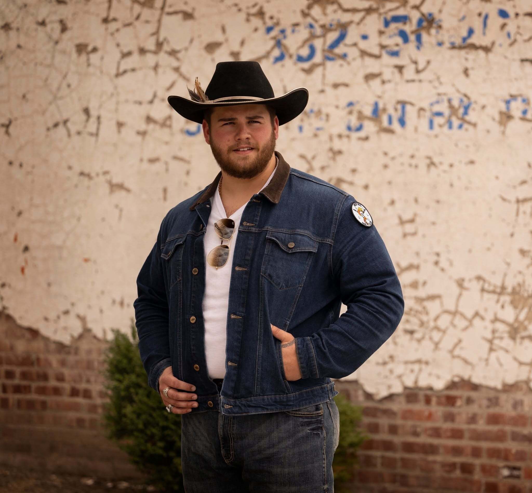 A photo of Tyler Anthony posing in front of a cement rustic wall 