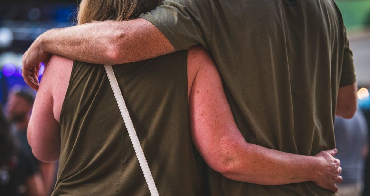 man an woman standing side to side with their arms around each other's back facing away from the camea