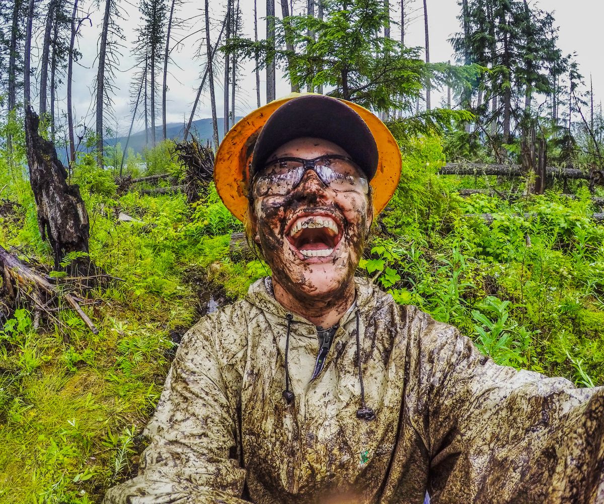 [Image Description: An MCC member jubilantly smiling in a selfie, covered in mud from head torso, wearing a hard hat and safety classes.]