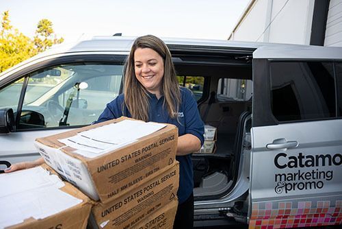 Woman standing outside loading mail trays into delivery van