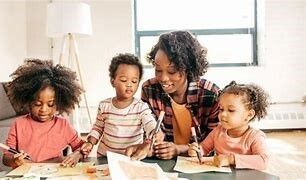 Woman sits with her three children working on a craft activity. 
