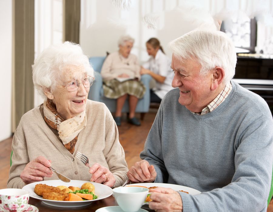 Female and male older adults sitting around a table and enjoying a meal, smiling at each other