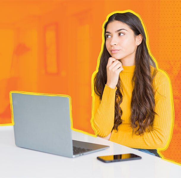 Person in a yellow sweater sitting with a laptop and smartphone against an orange background.