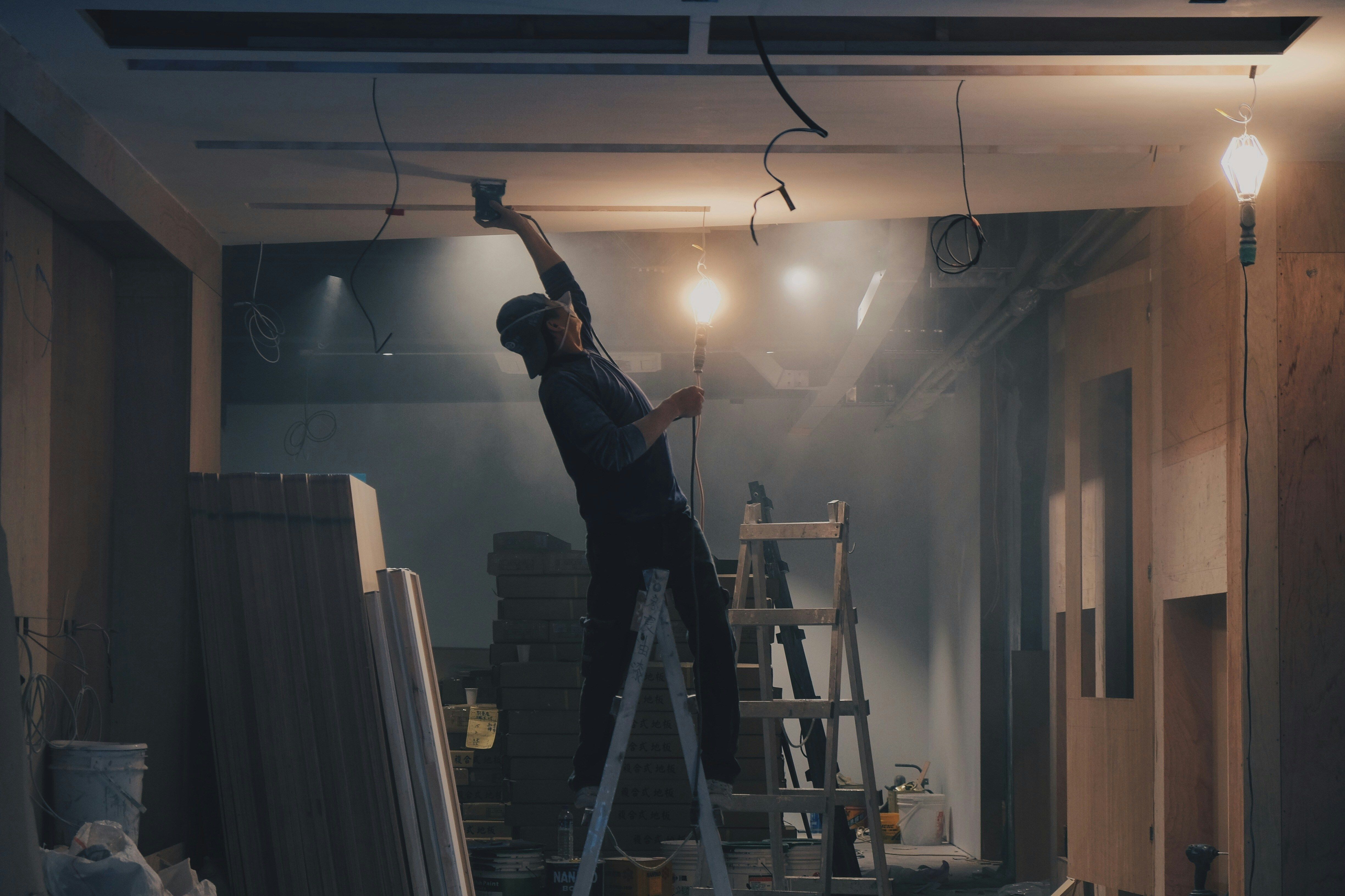 photo of a man on a ladder sanding drywall.