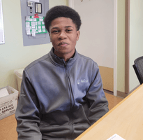 A young man sits at a desk wearing an Atlantic Health System light-weight zip-up