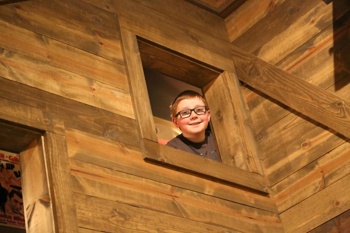 Boy looking out an open window of a boarded wall at the Smoky Hill Museum.