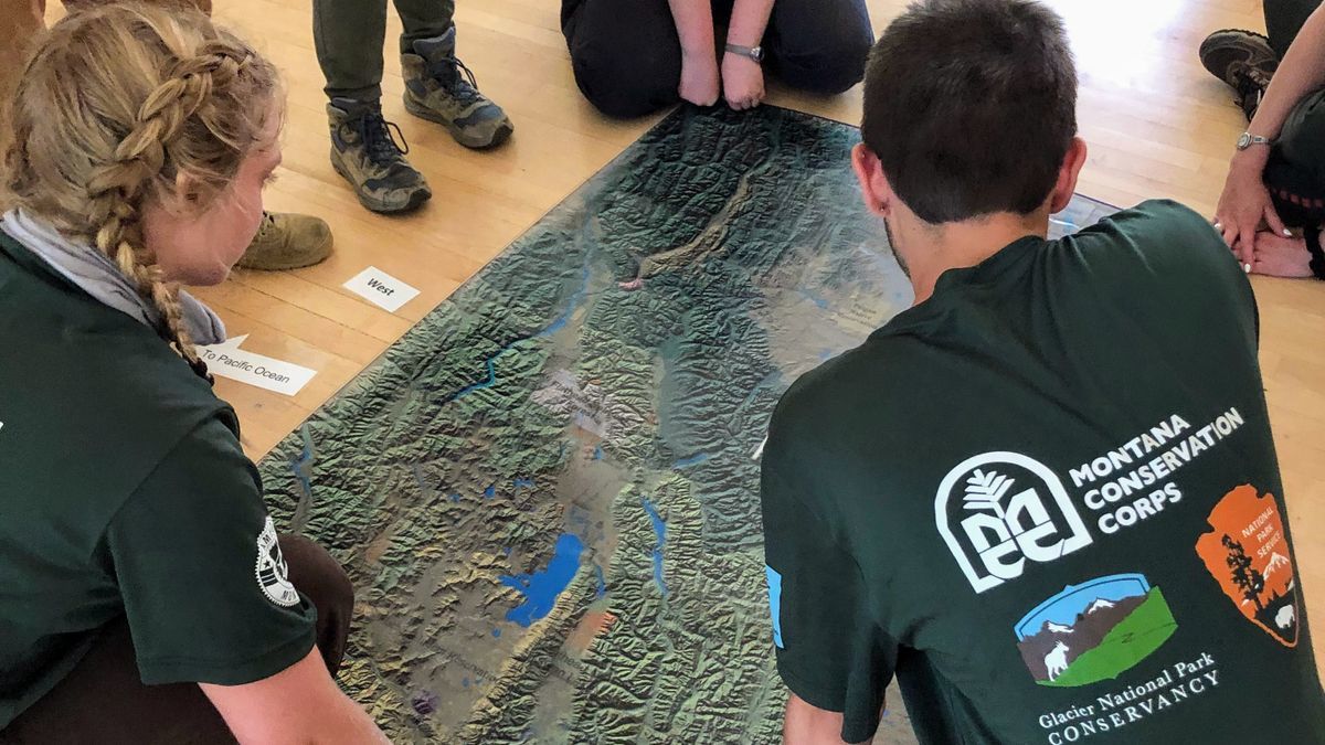 [Image Description: Looking down onto a map, two MCC youth members are on the ground viewing details for the mountain range they are studying.]