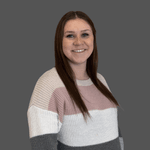 Brunette female with long hair smiling at the camera. She is wearing a light pink, cream, and gray striped sweater. The background is solid gray.