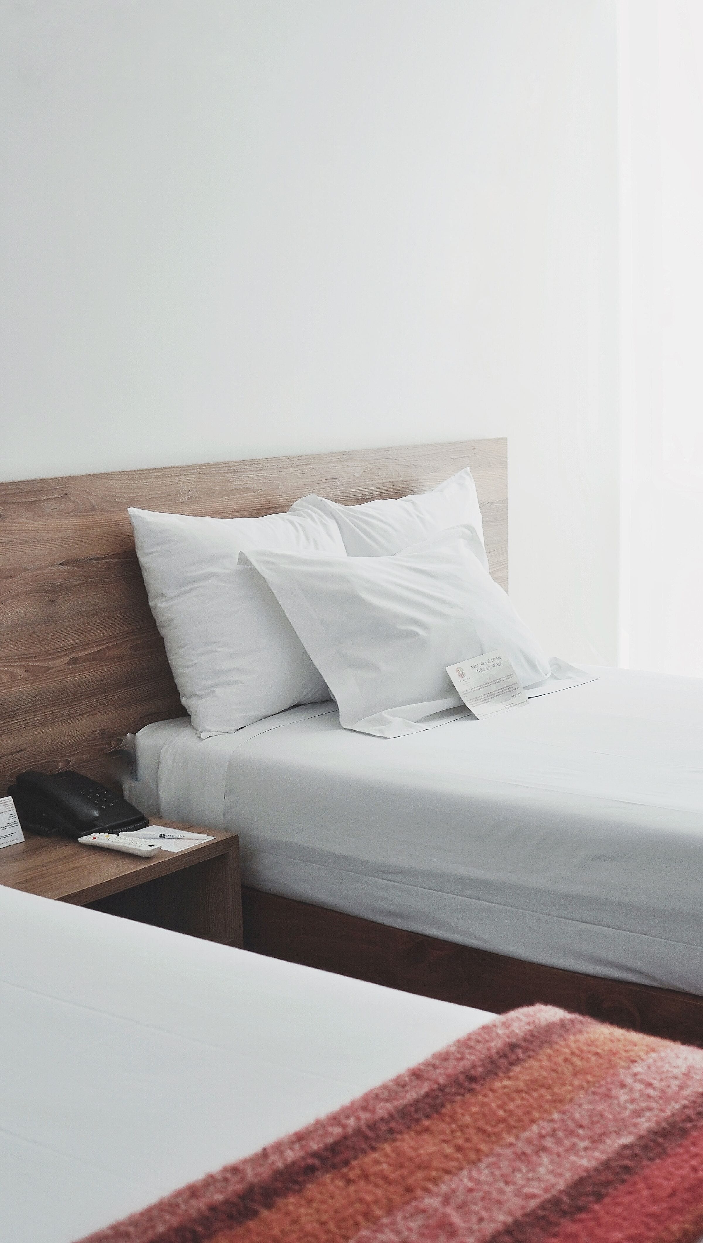 Image of a hotel room with a white bed with three white pillows propped against a brown headboard