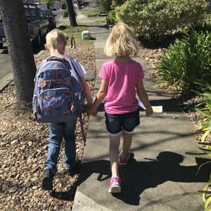 brother wearing backpack and sister walk away holding hands