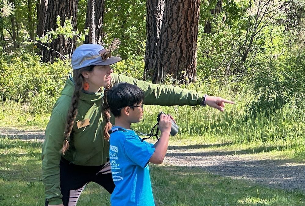 A WRI Field Educator assisting a student with finding a bird with their binoculars.