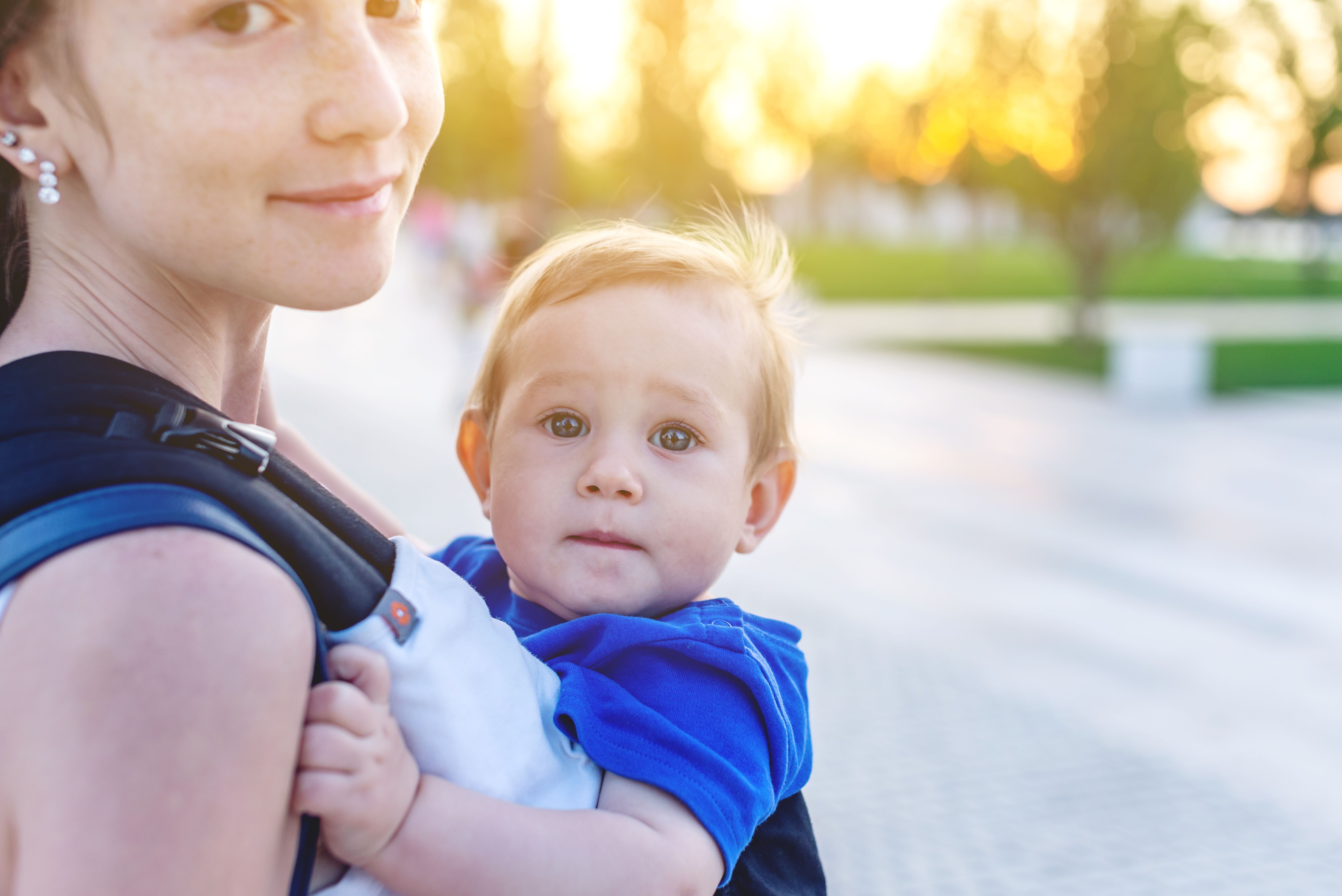 Photo of young mom holding baby in her arms looking into the camera with a soft smile. 