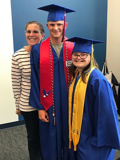 Two students in graduation cap and gowns with their teacher.