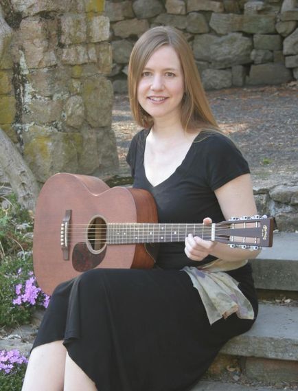 a photo of musician Heather Mulvey sitting down and holding an acoustic guitar. 