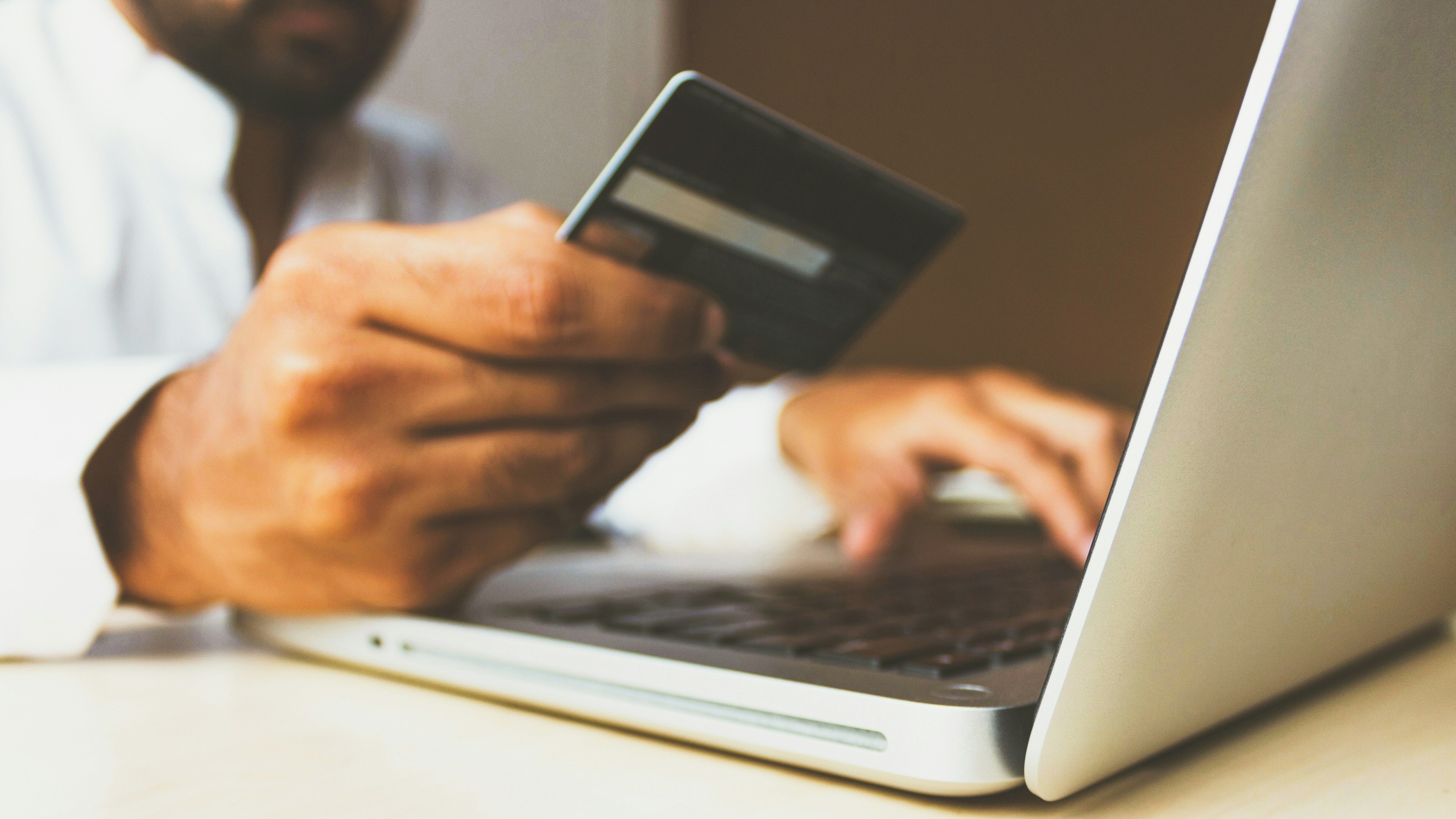 A man holds a credit card while typing on a laptop