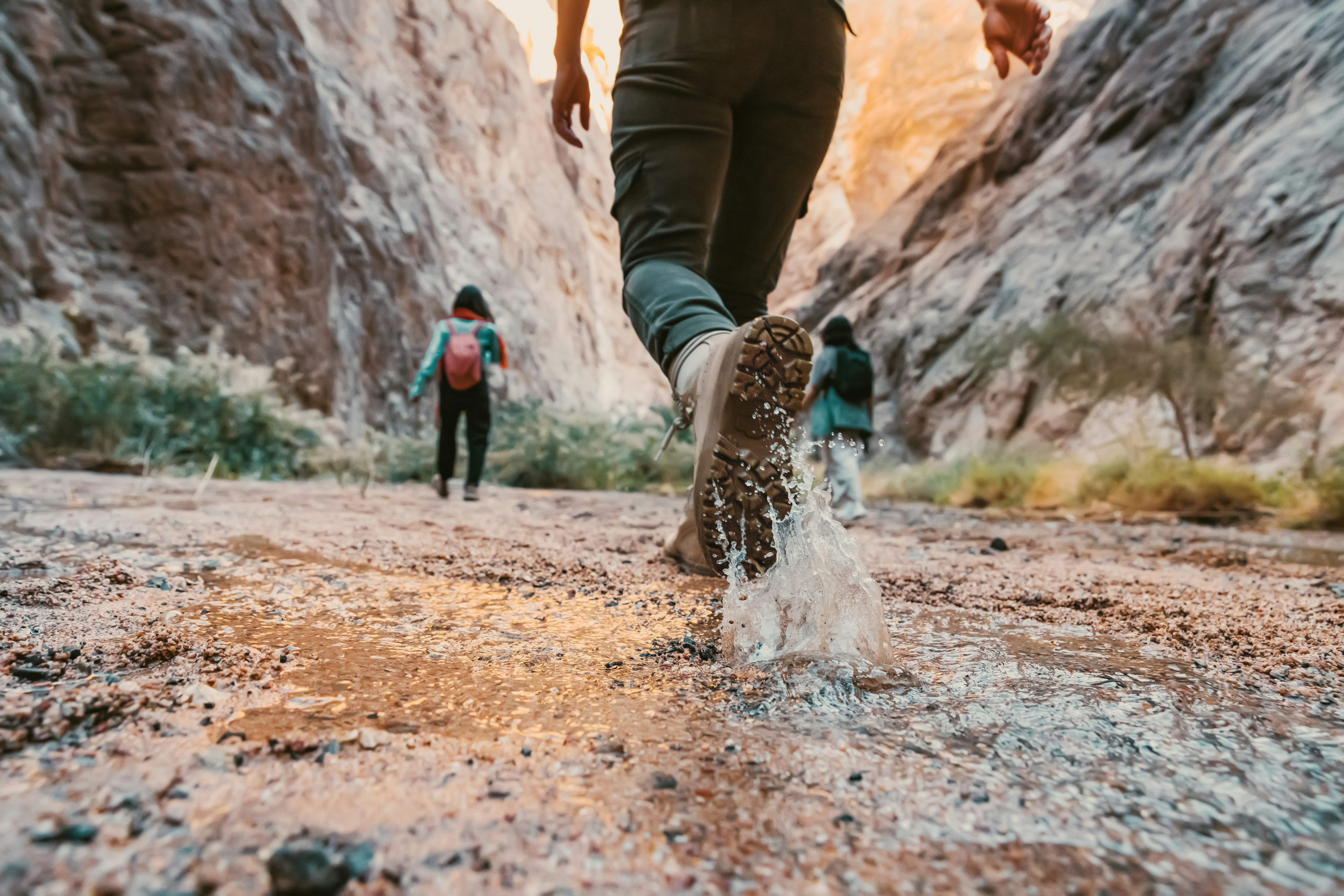 photo of people hiking up a shallow river through a canyon