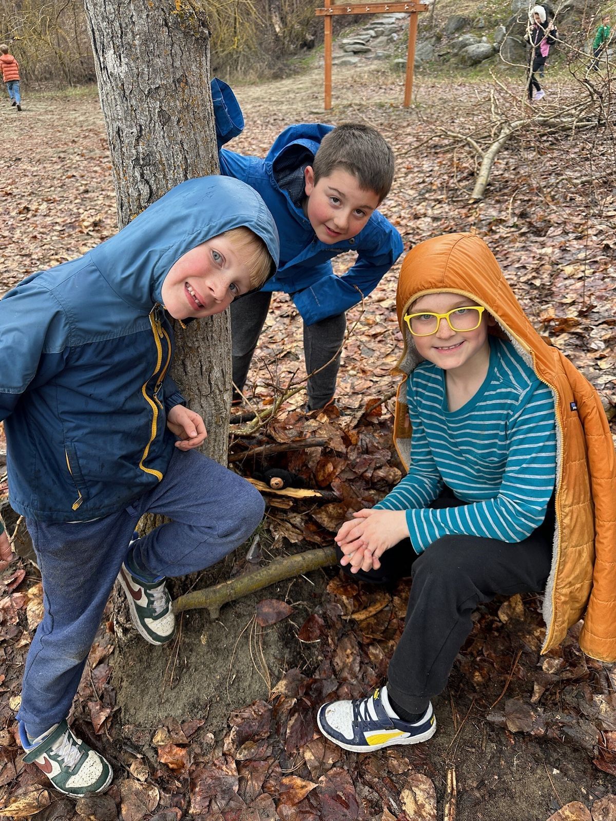 Three boys pose for the camera with their hoods up with the woods in the background.