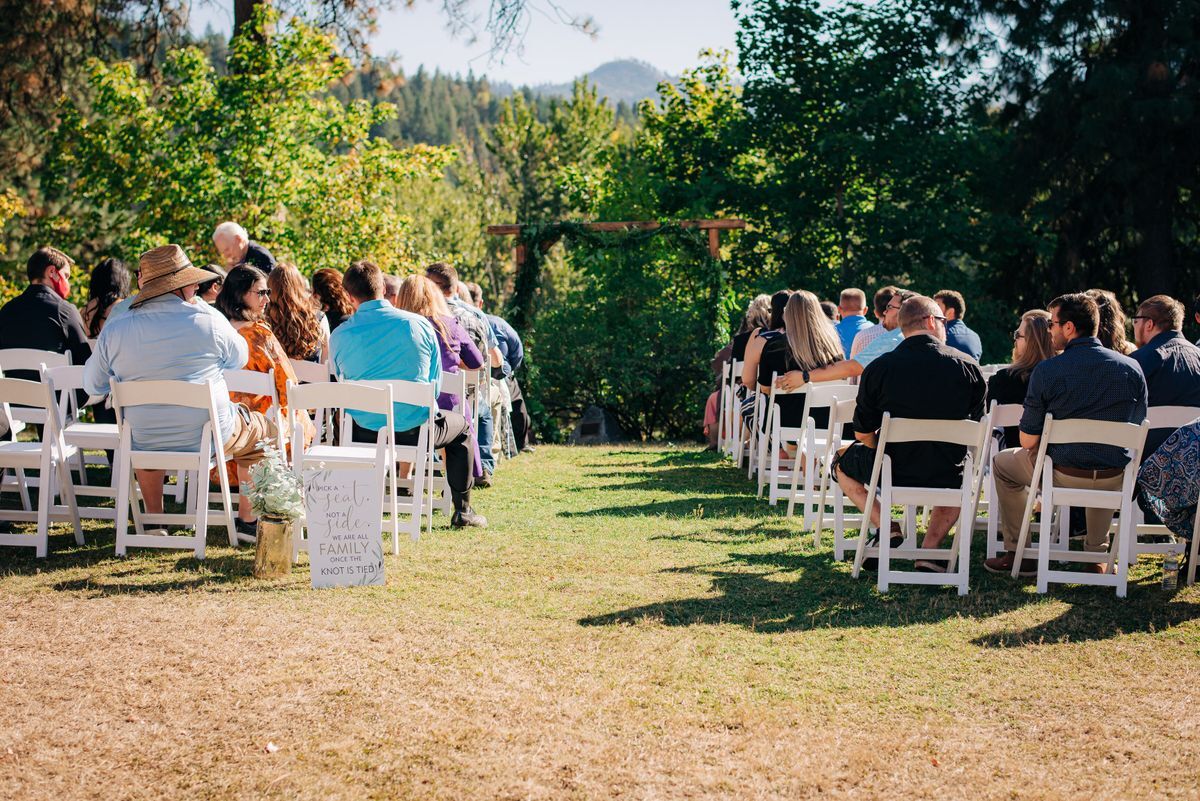 A scenic image of a wedding ceremony set up on the lawn with rows of people seated in white chairs facing an alter.