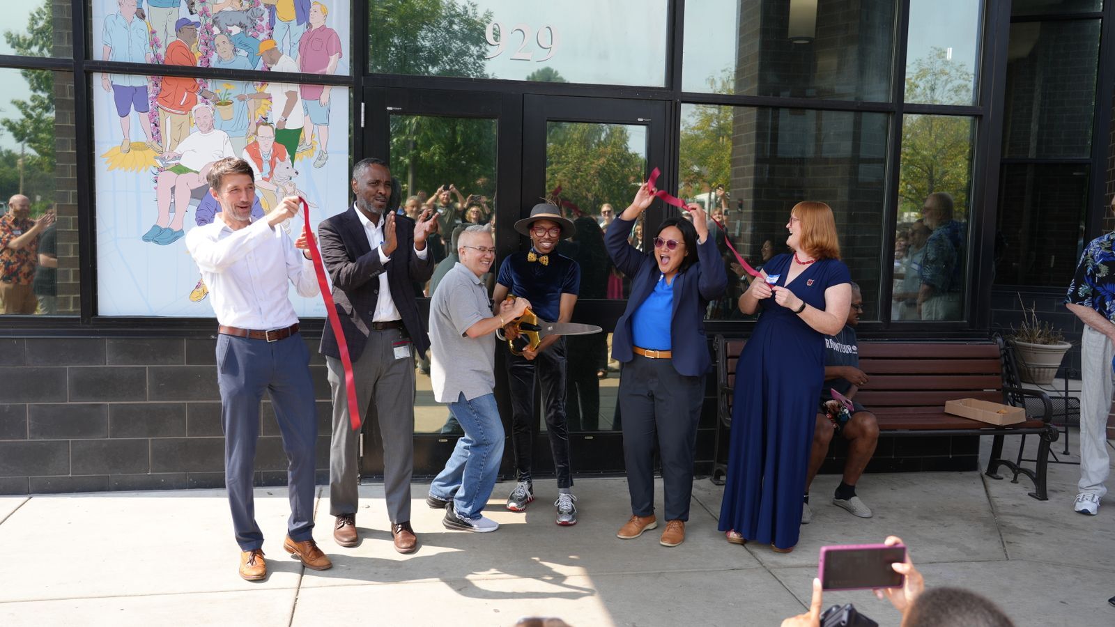 People cutting a ribbon in front of a door and smiling