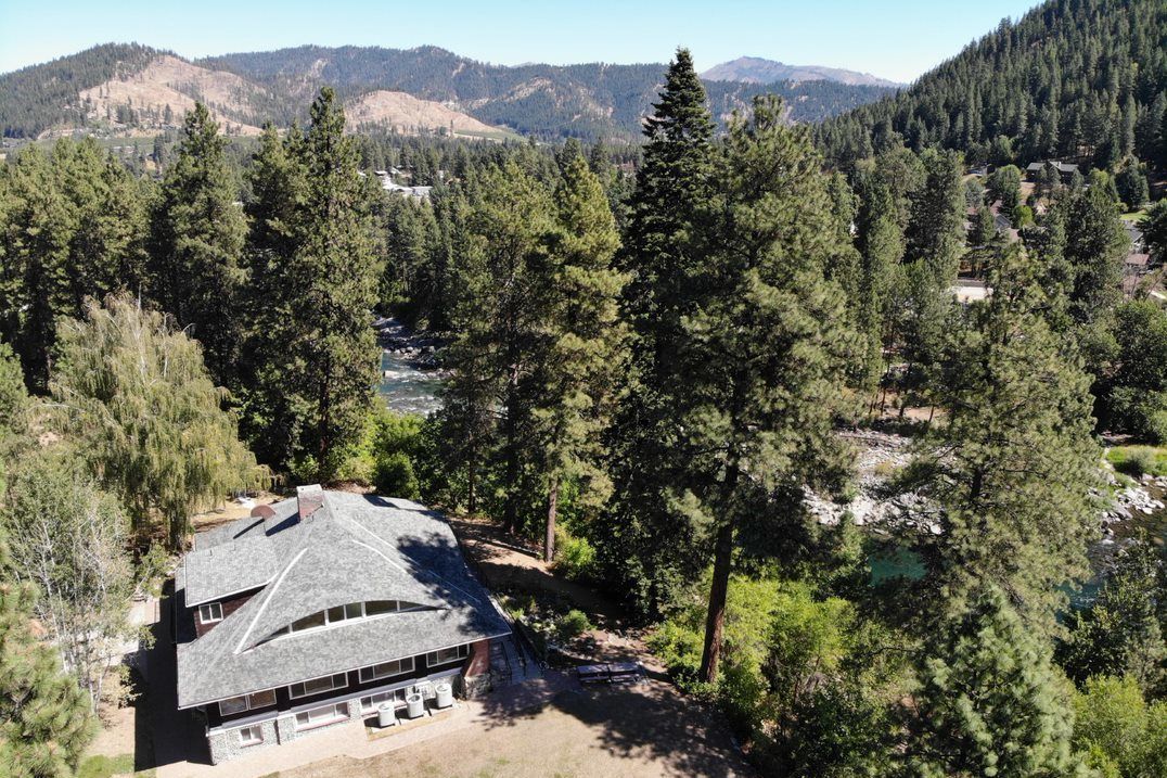 A drone image of a brown building set amongst the trees and river.