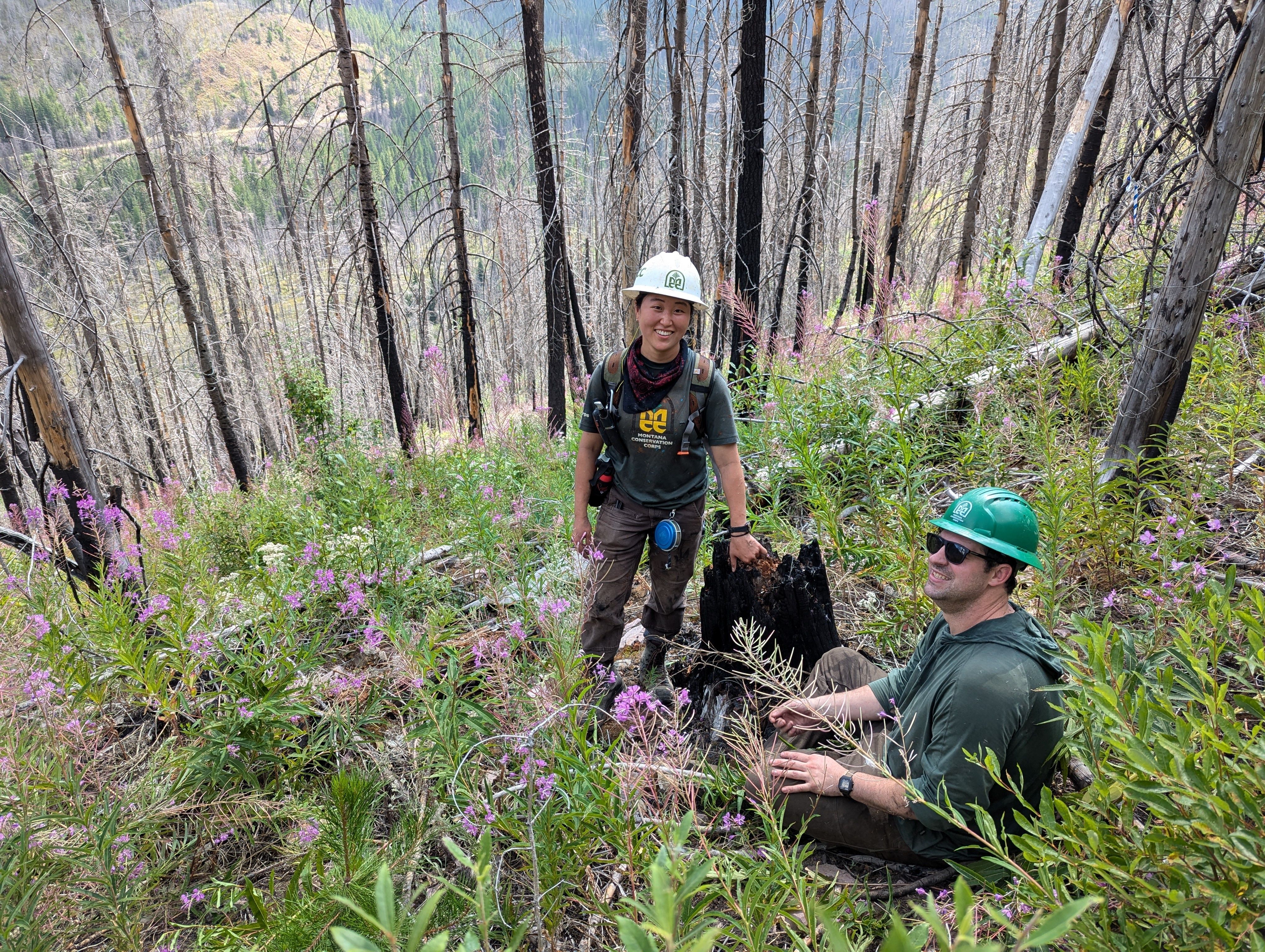 A crew leader and a field coordinator sit on a hillside, smiling.