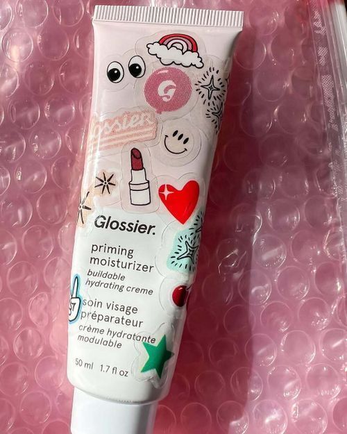 Glossier moisturizer tube decorated with playful brand stickers, an example of promotional stickers for business in beauty packaging.