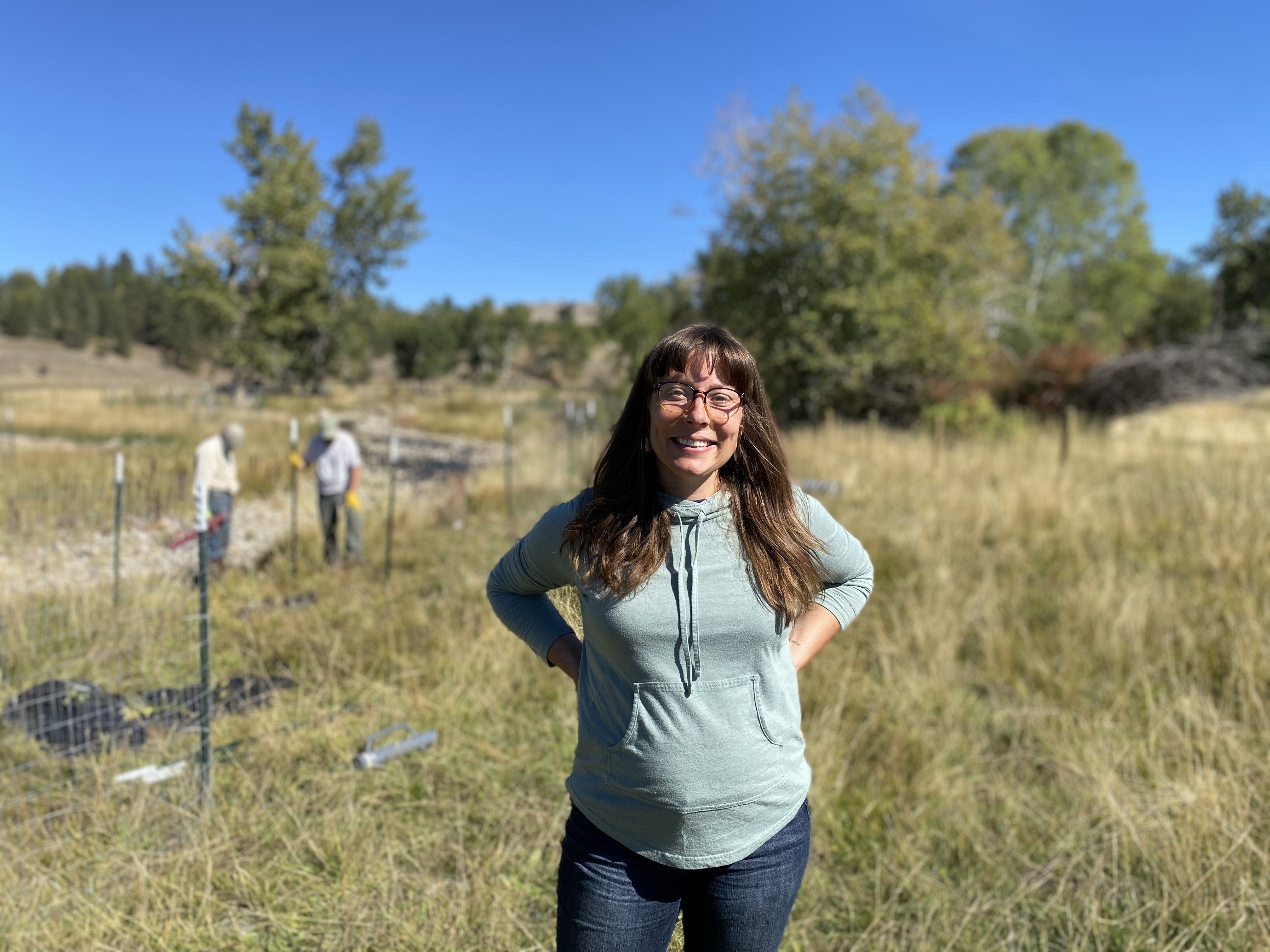 A woman, Heather, stands in a field smiling at the camera