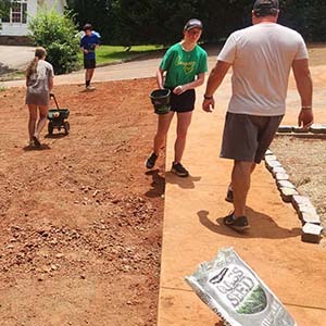 Volunteers shoveling and moving dirt with a wheelbarrow on a hillside