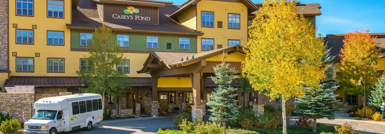 Entrance to a building named "Casey's Pond" with a shuttle bus in front and bright autumn trees.