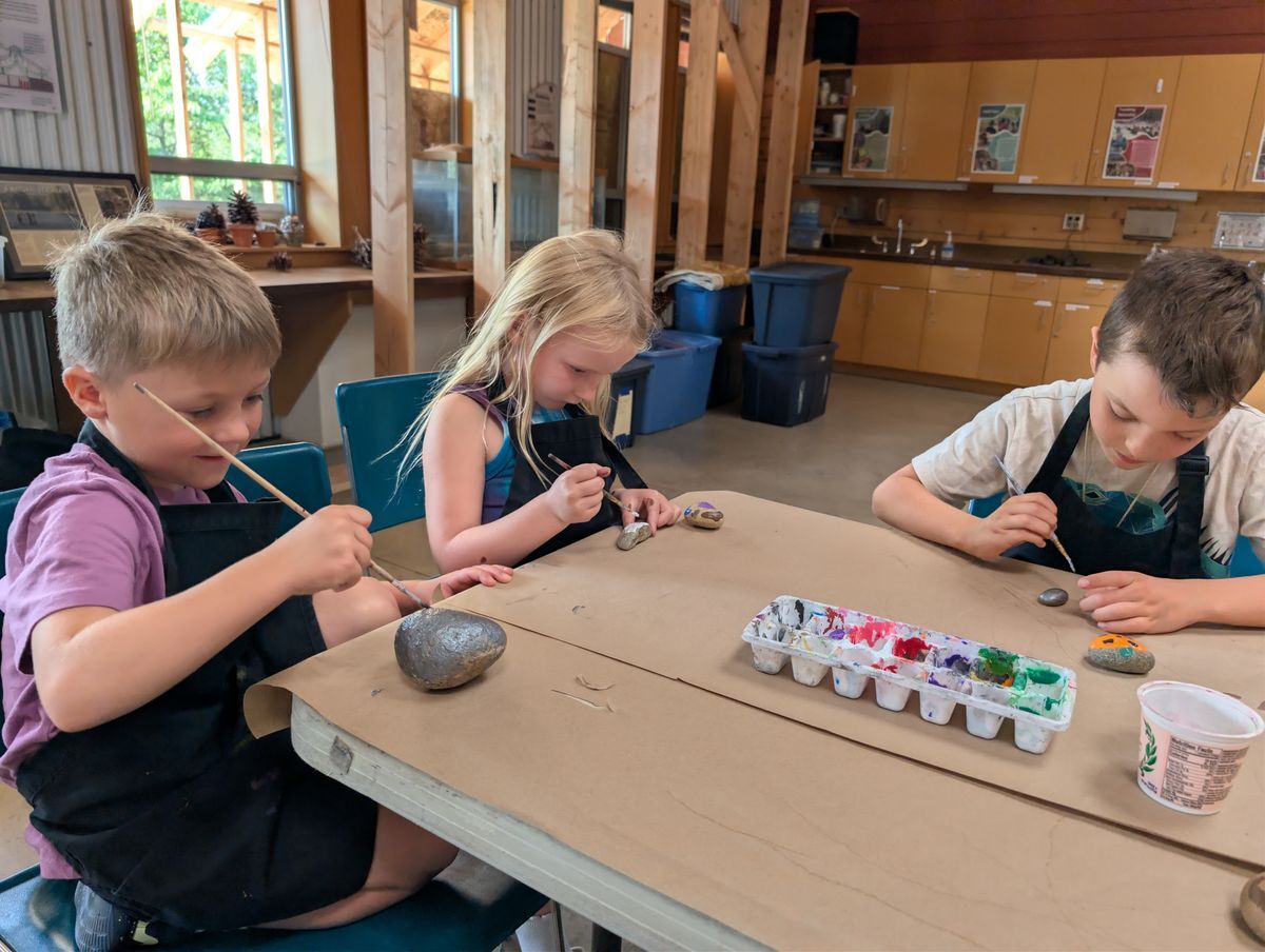 Three students painting rocks inside the Red Barn during Amazing Artists Camp.