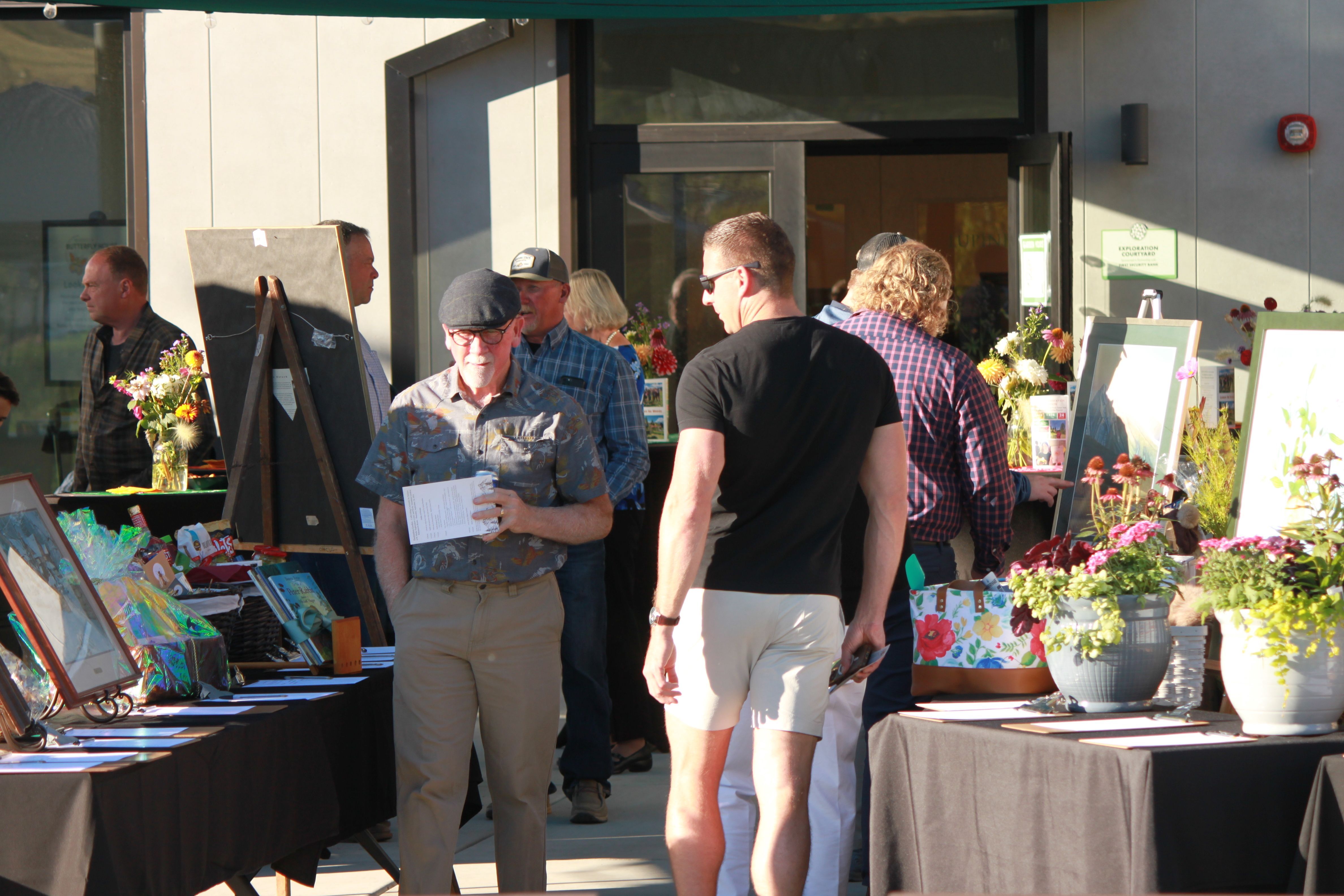 A crowd walks through an outside display of auction items including paintings.