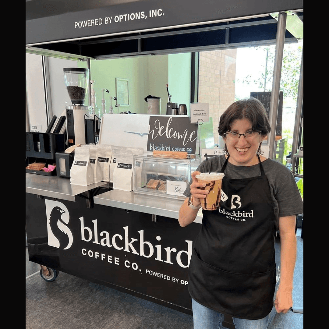 An employee holding coffee in front of the Blackbird Coffee Co stand. 