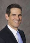 Photo of Dr. Christopher Bowlus wearing a blue tie, black suit, and smiling at the camera