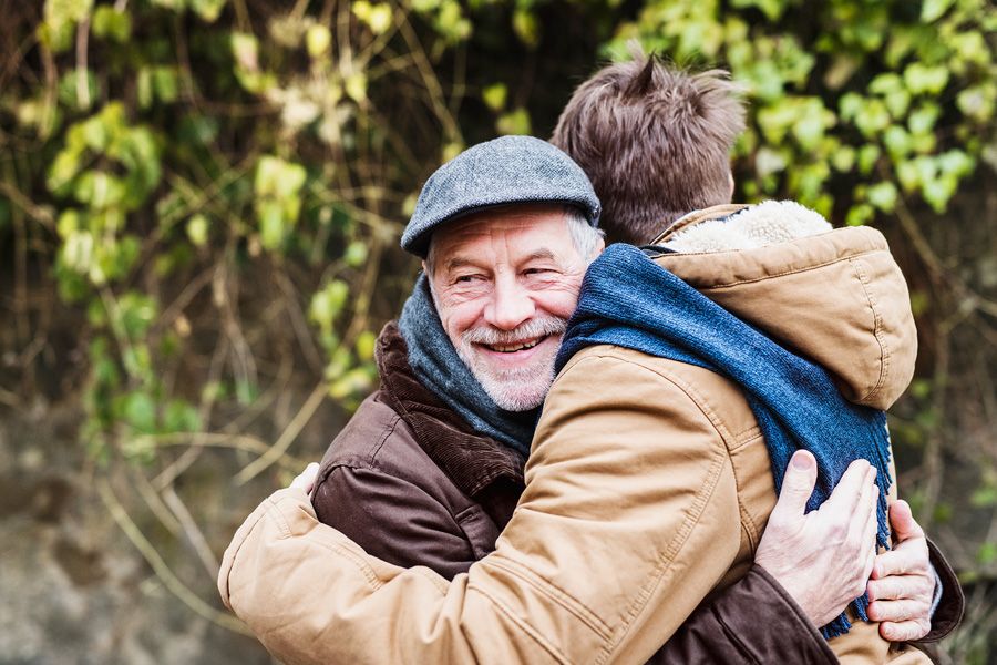 Older man smiling outside and hugging his adult son